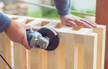 crop unrecognizable carpenter polishing wooden construction with grinding machine