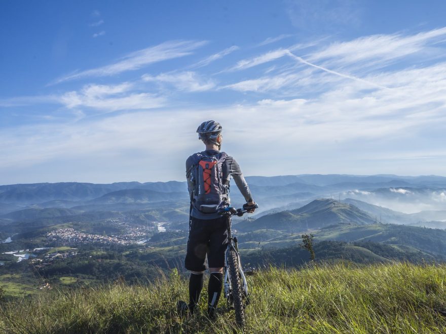 biker holding mountain bike on top of mountain with green grass