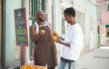 a seller talking to his customer while holding orange fruits