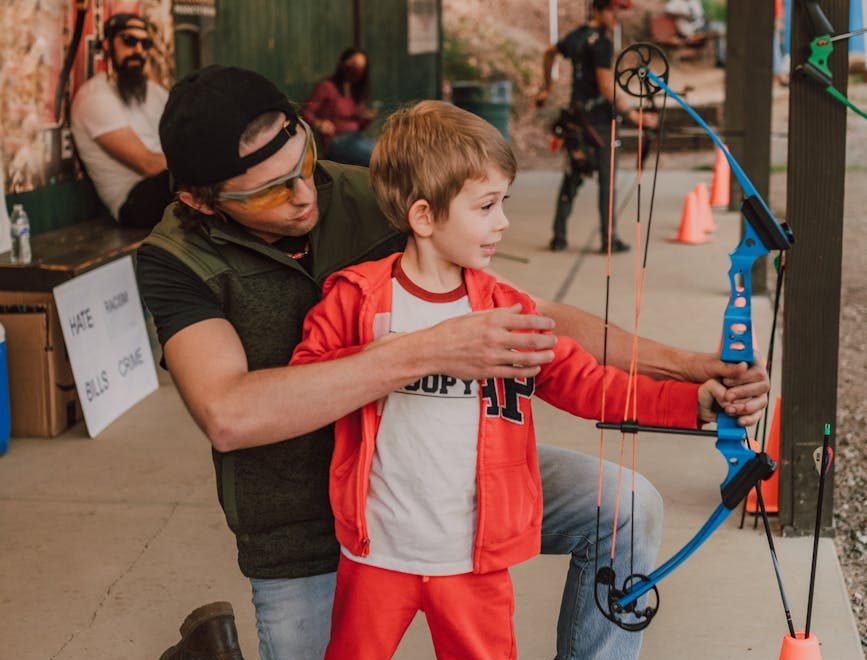 a man teaching a boy how to aim the arrow